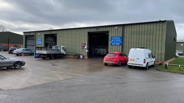 Exterior of Tockwith Mot Centre Ltd, featuring a large green industrial building, vehicles parked outside, and signage.