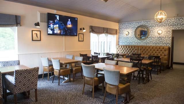 Cozy restaurant interior with wooden tables, chairs, patterned wallpaper, and a large TV on the wall.
