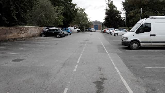 Free parking lot in Pocklington, Yorkshire, with parked cars, trees, and a building in the background under a cloudy sky.
