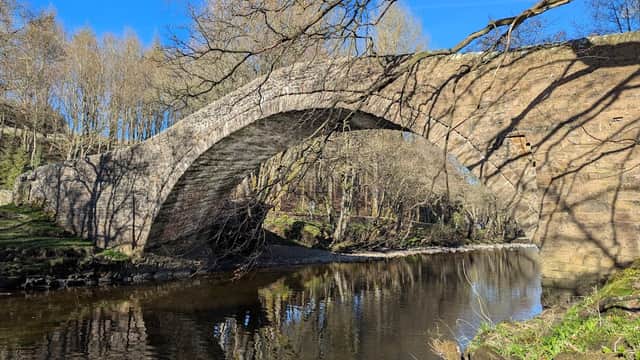 Stone arch bridge over a calm river, surrounded by bare trees and a clear blue sky.