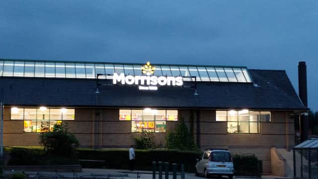 Morrisons store in Heckmondwike, Yorkshire, illuminated at dusk with a clear sky and parking area in front.
