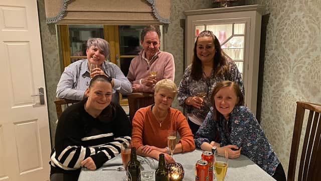 Group of six people smiling at a table with drinks, in a cozy, well-decorated indoor setting.