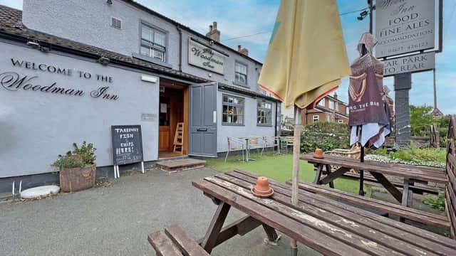 Welcome to The Woodman Inn, featuring outdoor seating, a yellow umbrella, and a sign for food and fine ales.