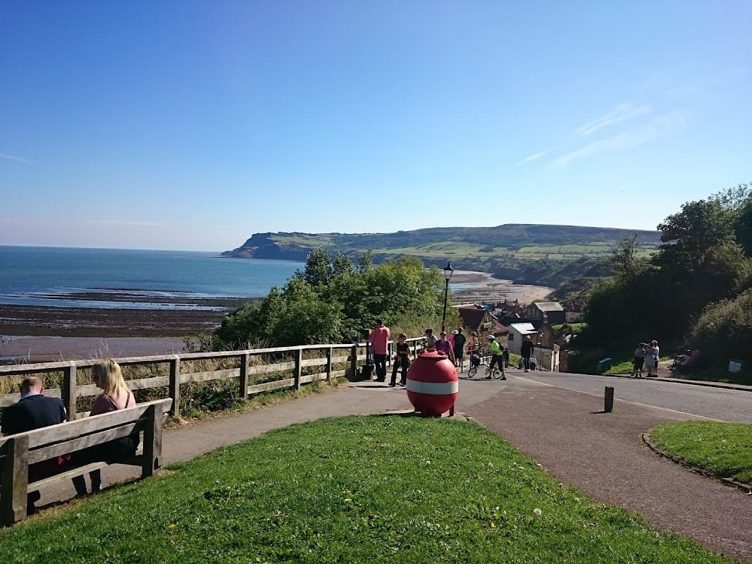 View of Bank Top Car Park with benches, a red pay display machine, and scenic coastline under a clear blue sky.