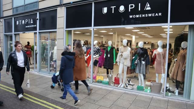 Shopfront of Utopia Womenswear featuring mannequins in stylish clothing, with shoppers walking by on the street.
