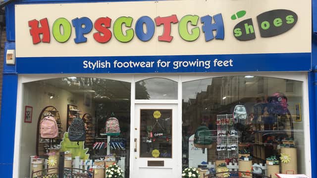 Bright shopfront with "HOPSCOTCH shoes" sign, showcasing colorful footwear and backpacks in the window display.