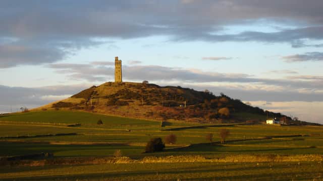 Victoria Tower atop Castle Hill, surrounded by rolling green fields under a dramatic cloudy sky.