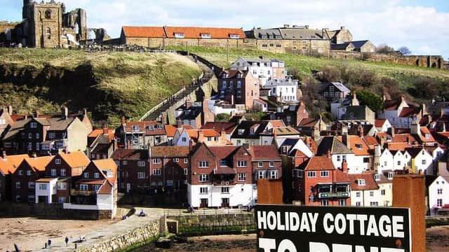 Holiday cottages with red-tiled roofs, a hilltop church, and a sign reading "Holiday Cottage To Rent" in Whitby.