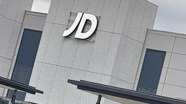 JD Sports store front with a large "JD" sign, surrounded by parked cars and a cloudy sky.