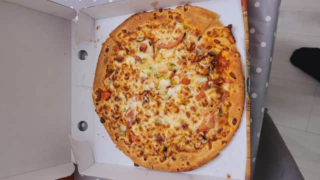 A pizza with melted cheese, tomatoes, and green peppers in a pizza box, resting on a polka dot tablecloth.