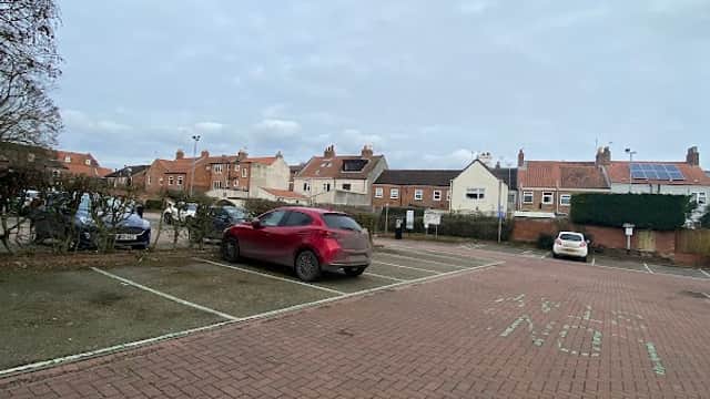 Bishops Manor House car park with empty spaces and nearby buildings under a cloudy sky.
