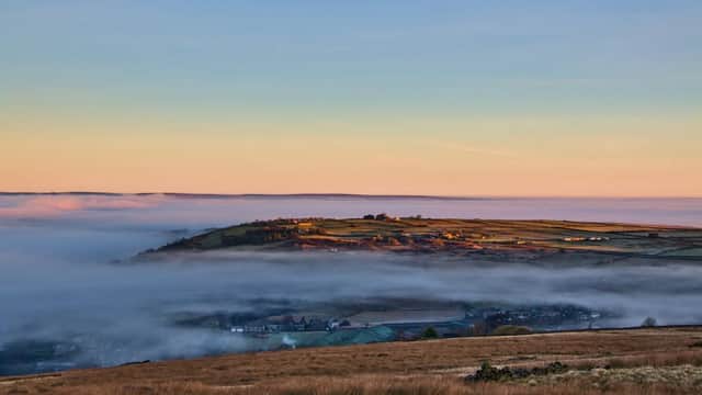 Rolling hills and valleys shrouded in mist, with a soft sunrise illuminating the landscape in Oxenhope, Yorkshire.