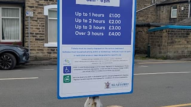 Signpost displaying parking charges and operating hours for Wesley Place Car Park in Silsden, Yorkshire.