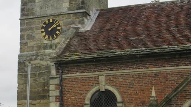 Church tower with clock, stone and brick walls, and a bench in front, set in a grassy area in Thorganby, North Yorkshire.