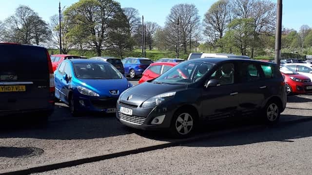 Main car park at Roundhay Park, featuring several parked cars and trees in the background under a clear blue sky.