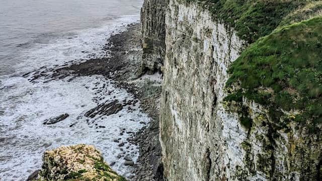 Dramatic cliffs at Bartlett Nab, overlooking the sea with grassy edges and waves crashing against the rocks below.