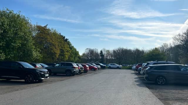 A spacious car park with various parked cars, surrounded by trees and a clear blue sky in Liversedge, Yorkshire.