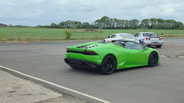 A bright green sports car and a white car parked on a tarmac near grassy fields at Tockwith Airfield.