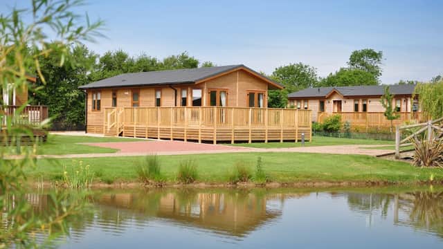Wooden lodges with decks by a tranquil pond, surrounded by greenery in Balk, North Yorkshire.