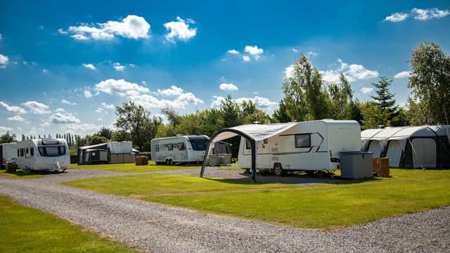 Caravans and tents set on a grassy area under a bright blue sky with scattered clouds at York Meadows Caravan Park.