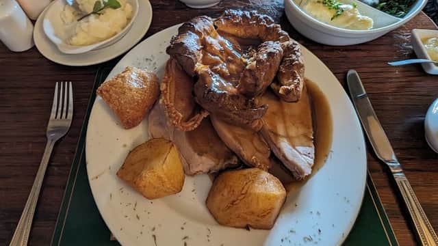 A plate of roast meat with Yorkshire pudding, roast potatoes, and gravy, surrounded by side dishes at a cozy pub table.