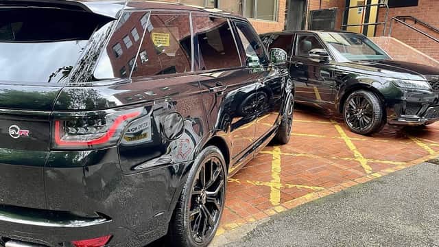 Two sleek black SUVs parked on a brick surface, showcasing shiny detailing and a clean exterior.
