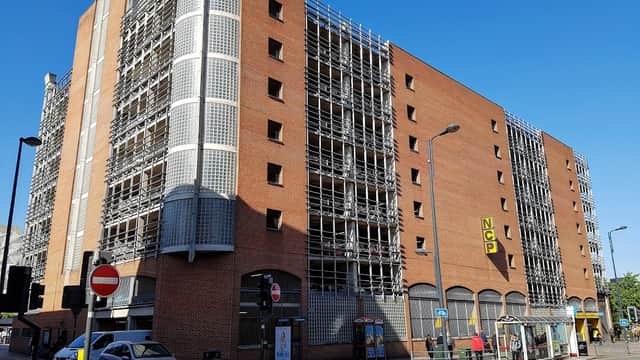 NCP Leeds The Markets car park with brick facade, scaffolding, and clear blue sky. Buses and cars in foreground.