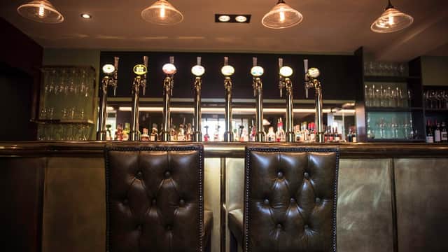 Elegant bar area with polished taps, glassware, and stylish leather stools under warm pendant lighting.