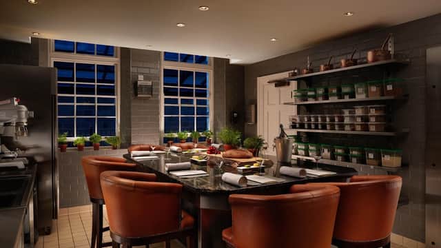 Modern kitchen with dark countertops, leather chairs, large windows, and shelves filled with jars and potted herbs.