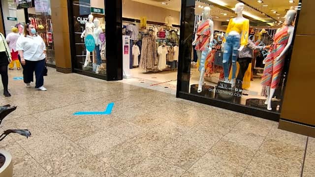 Storefront of Quiz Clothing featuring mannequins in colorful outfits, shoppers, and a modern interior in a mall setting.