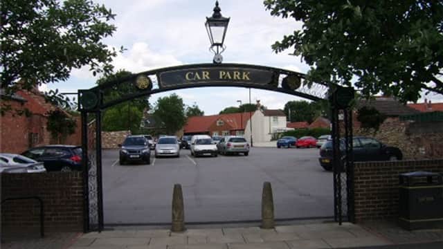 Entrance to Market Hill Car Park with a decorative arch, trees, and parked cars in a spacious lot.