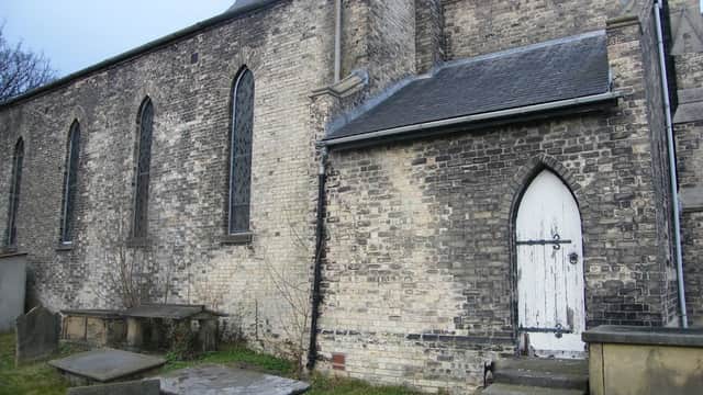 St John the Baptist Church features a stone exterior, arched windows, a white door, and adjacent gravestones.