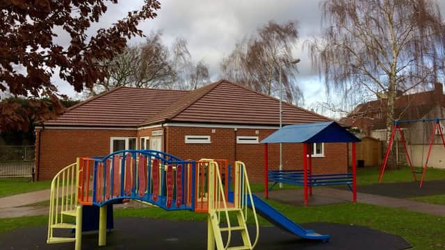 Community centre with a playground featuring a slide, bridge, and swings, surrounded by trees and cloudy skies.
