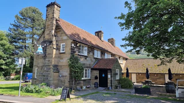 Charming stone building with a red-tiled roof, surrounded by greenery and outdoor seating, in a sunny Yorkshire setting.