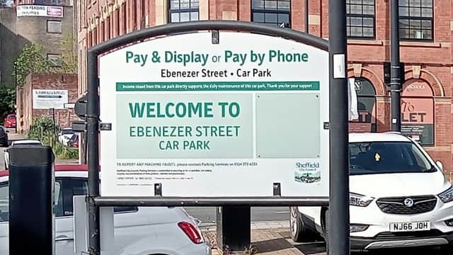 Sign for Ebenezer Street Car Park with parking instructions, surrounded by buildings and parked cars.