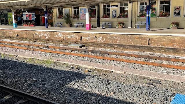Harrogate Station platform with waiting area, train tracks, and nearby buildings under a clear blue sky.