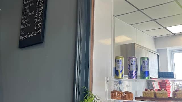Menu board with coffee prices, a glass display case with pastries, and a small plant on a marble counter.