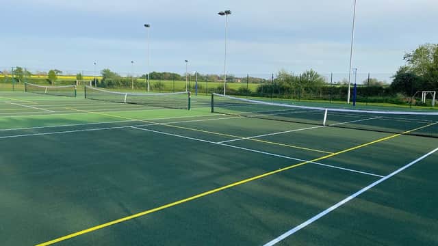 Tennis courts with nets and markings, surrounded by greenery and a clear sky at Stamford Bridge Tennis Club.