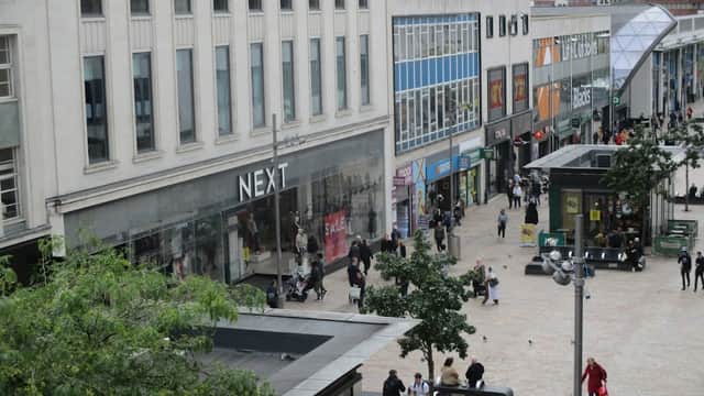 Shopping center with various stores, pedestrians, and greenery; modern architecture and a busy atmosphere in Sheffield.
