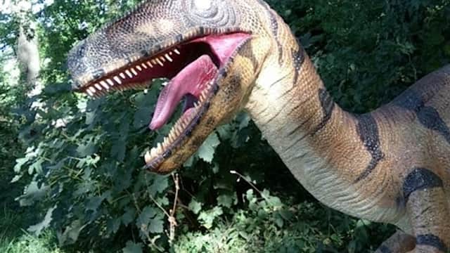 A large, realistic dinosaur sculpture among lush greenery, showcasing vibrant colors and intricate details.