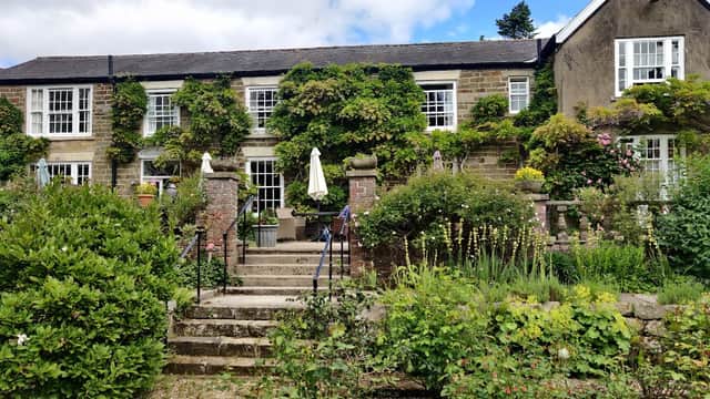 Charming country house hotel with lush greenery, stone steps, and outdoor seating under umbrellas in Lastingham, Yorkshire.