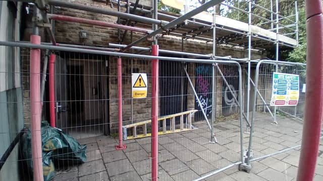 Scaffolding surrounds a stone building with a "Danger" sign and a safety notice, indicating ongoing construction.