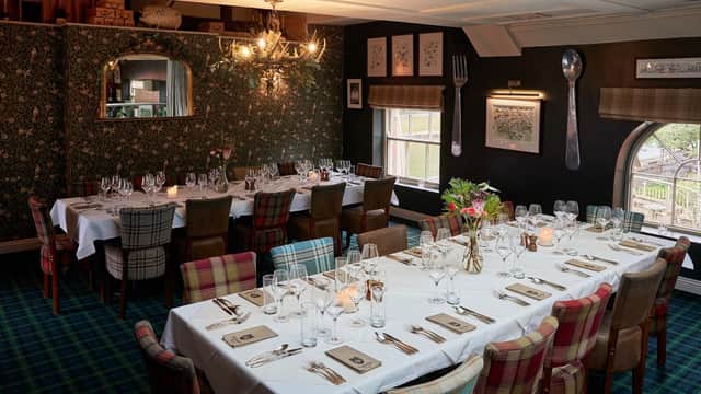Elegant dining setup with checkered chairs, white tablecloths, and floral wallpaper in a cozy restaurant interior.