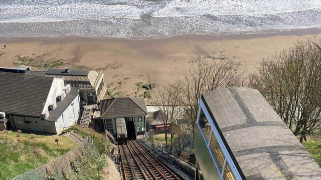 Cliff Lift tracks descend toward the beach, with the sea and sandy shore visible below, framed by greenery.