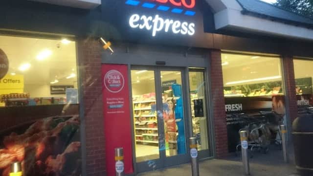 Tesco Express storefront with bright signage, shopping carts outside, and visible grocery displays inside.