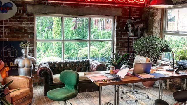Vintage interior with a neon "FUNHOUSE" sign, leather sofa, green chair, and a desk with a laptop and plants.