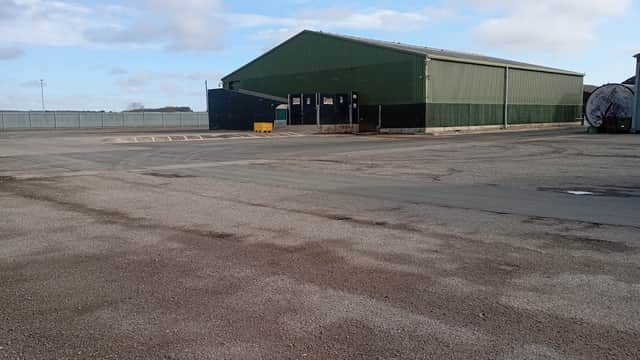 Large green warehouse building with a gravel parking lot and cloudy sky in the background.