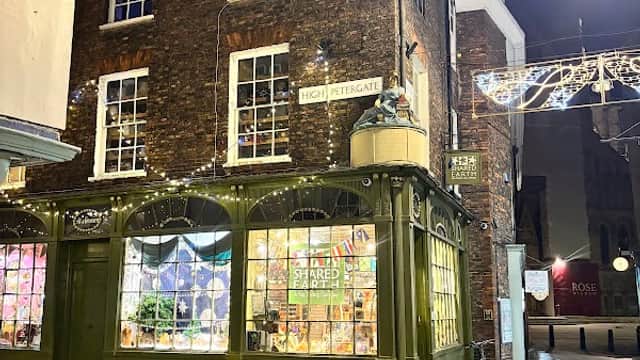 Charming gift shop with green faΓ§ade, fairy lights, and colorful displays, located on a cobblestone street at night.
