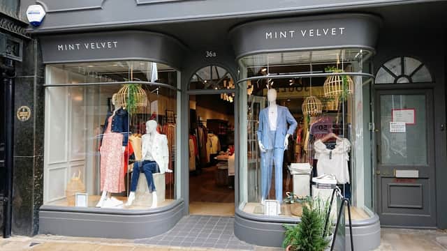 Two curved shop windows displaying clothing and accessories, with mannequins and green decor, at Mint Velvet in Harrogate.
