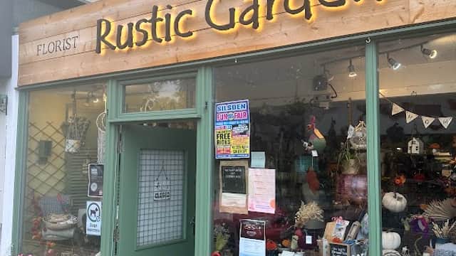 Rustic Garden florist storefront with wooden sign, colorful flowers, and decorative items in window display.